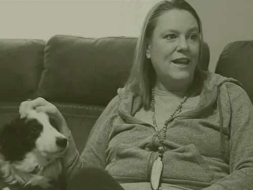 A woman sitting on a couch petting a dog