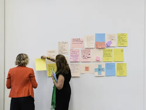 Two people in front of post it notes on a white wall