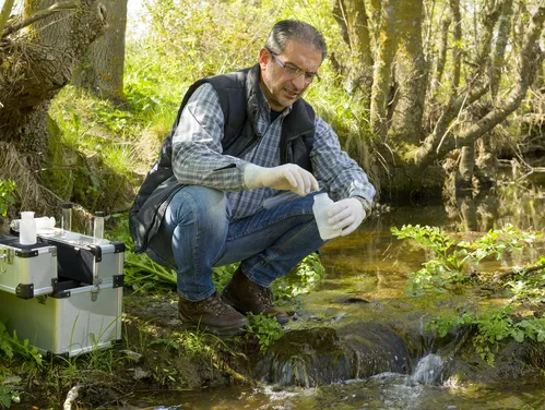 Quality technician sampling water from stream