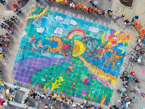 Aerial view of a large sidewalk chalk drawing that says Woodstock with a crowd of spectators