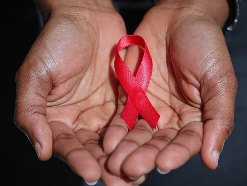 Hands holding a red AIDS advocacy ribbon