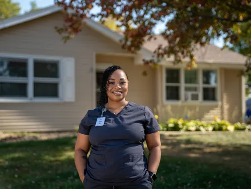 Woman in scrubs standing in front of her home