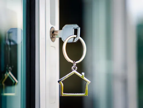 Keys in a door with a keychain shaped like a house icon