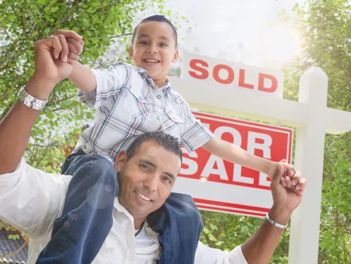 Boy on a man's shoulders in front of a SOLD sign