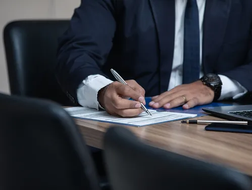 Close up of man signing documents with pen next to a laptop computer
