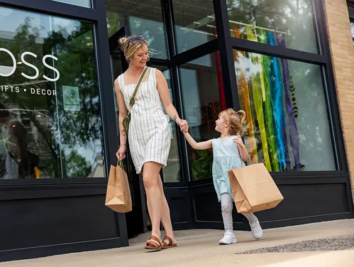 woman and daughter walking in front of  store with shopping bags