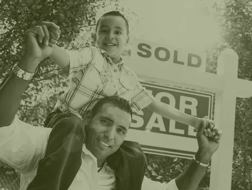 Boy sitting on dad's shoulders in front of For Sale/Sold sign