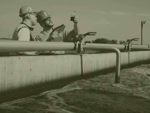 Two technicians in hard hats looking at water sample