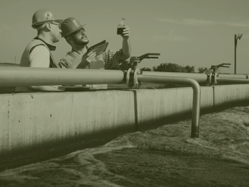 Two technicians in hard hats looking at water sample