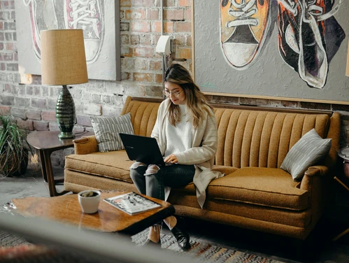 Woman sitting on tan couch, working on laptop