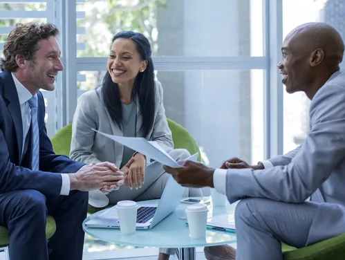 Three businesspeople sitting in green chairs at a low glass table 