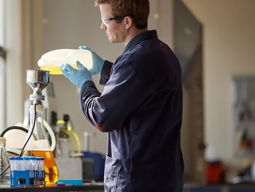 Man in coveralls pouring liquid into a large glass beaker
