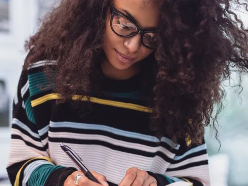 Woman in striped sweater and wearing glasses writing in a notebook
