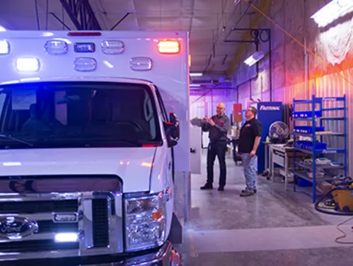 Two men standing next to a white ambulance in a garage setting
