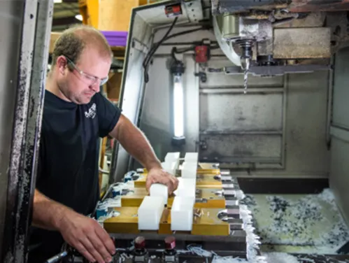 Person wearing a dark tee and safety glasses working with machining equipment