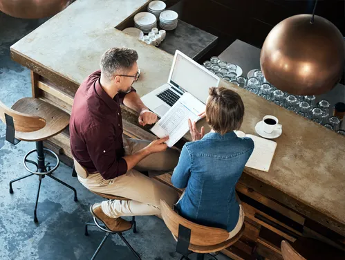 Two people sitting with a laptop and coffees working together at a counter