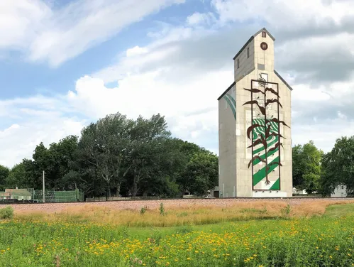 White milk carton-shaped grain elevator with an illustration of green field stripes and a brown corn stalk
