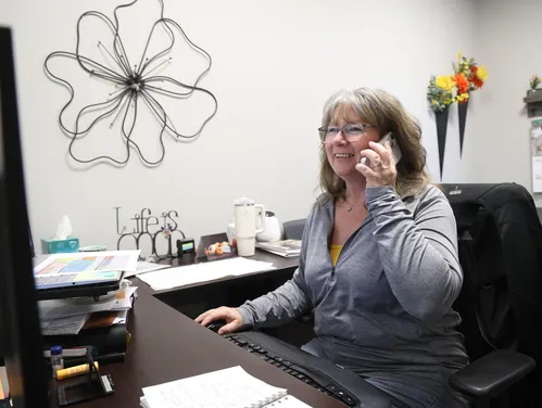 Woman with a cellphone at her ear sitting at a computer in an office setting