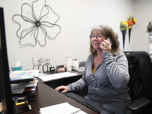 Woman with a cellphone at her ear sitting at a computer in an office setting