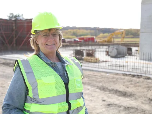A woman in a neon yellow hard hat and vest standing in front of a construction site