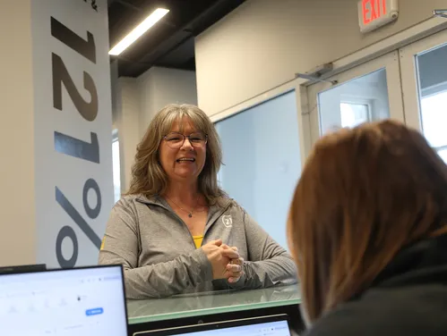 A woman standing in front of a reception desk with 121% on the wall behind her