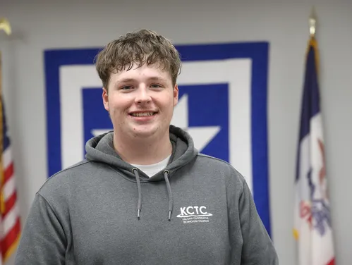 Young man in a hooded sweatshirt standing between Iowa and American flags