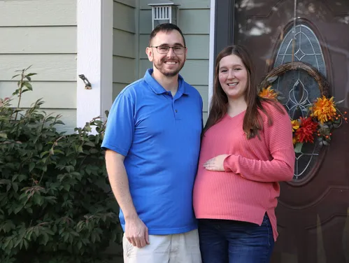 A man and a pregnant woman outside their home in front of a decorated door