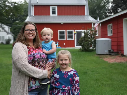 Woman and two children standing in a backyard with a red house behind them