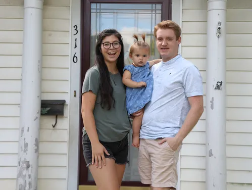 A woman, man and toddler standing in front of their house with columns and a glass door