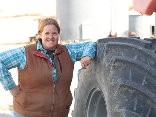 A female farmer standing next to a tractor tire