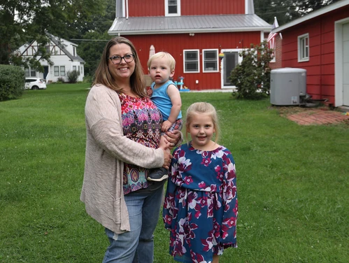 a family stands outside of their red house
