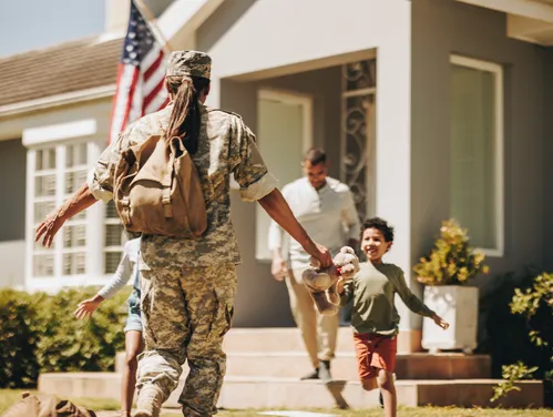 a person in a military uniform running to hug people in front of a home