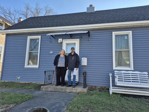 Couple standing in front of blue house with new roof 