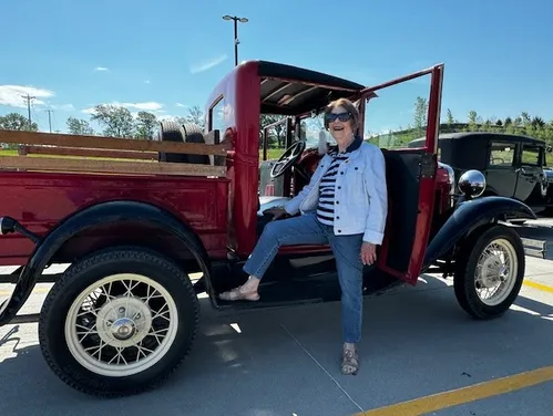 Woman Standing with her leg up on red pick-up truck.