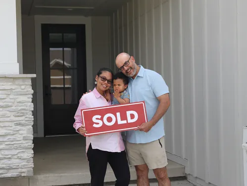 a family standing in front of a home holding a sign that says sold