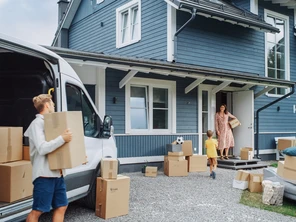 Person unloading boxes from a moving van in front of a blue house