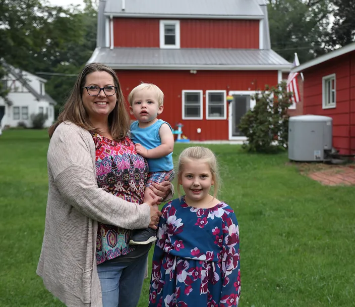 a woman and two kids standing in front of red house