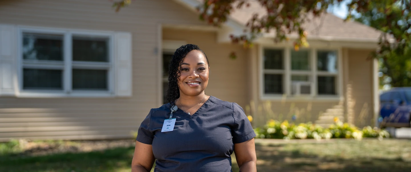 Woman in scrubs standing in front of her home