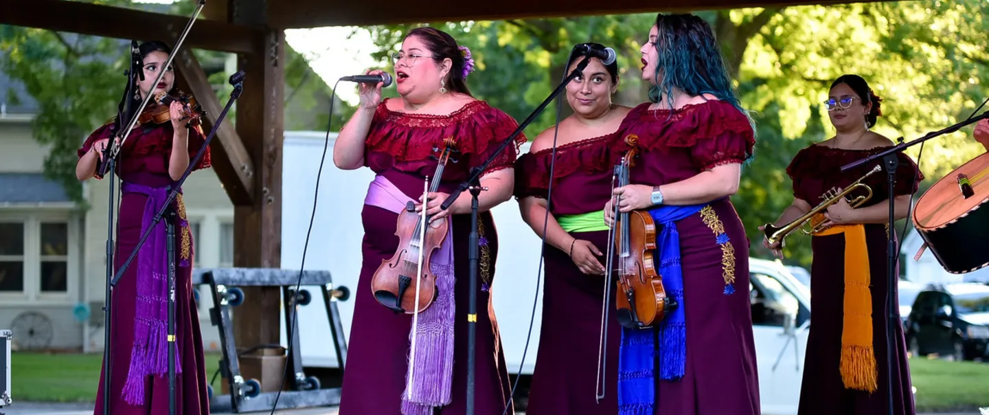 5 women performing music wearing red dresses on a stage