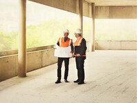 two people look at blueprints at a construction site