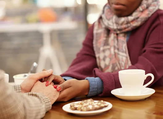 Two people gently hold hands over a table with coffee cups