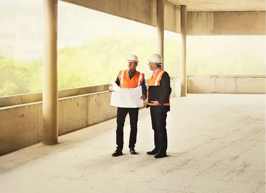 two people look at blueprints at a construction site