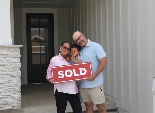 a family standing in front of a home holding a sign that says sold
