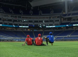 Three people sitting on the ground in an empty sports stadium