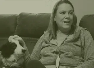 A woman sitting on a couch petting a dog