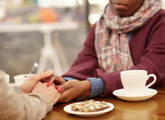 Two people gently hold hands over a table with coffee cups