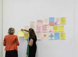 Two people in front of post it notes on a white wall