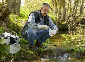 Quality technician sampling water from stream