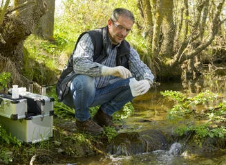 Quality technician sampling water from stream