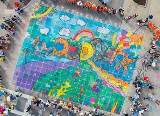 Aerial view of a large sidewalk chalk drawing that says Woodstock with a crowd of spectators